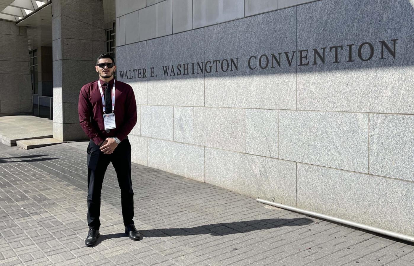 Basel Farhat standing infront of the Walter E. Washington Convention Center, wearing dress clothes and black sunglasses.