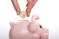 Hand putting coins into a piggy bank.