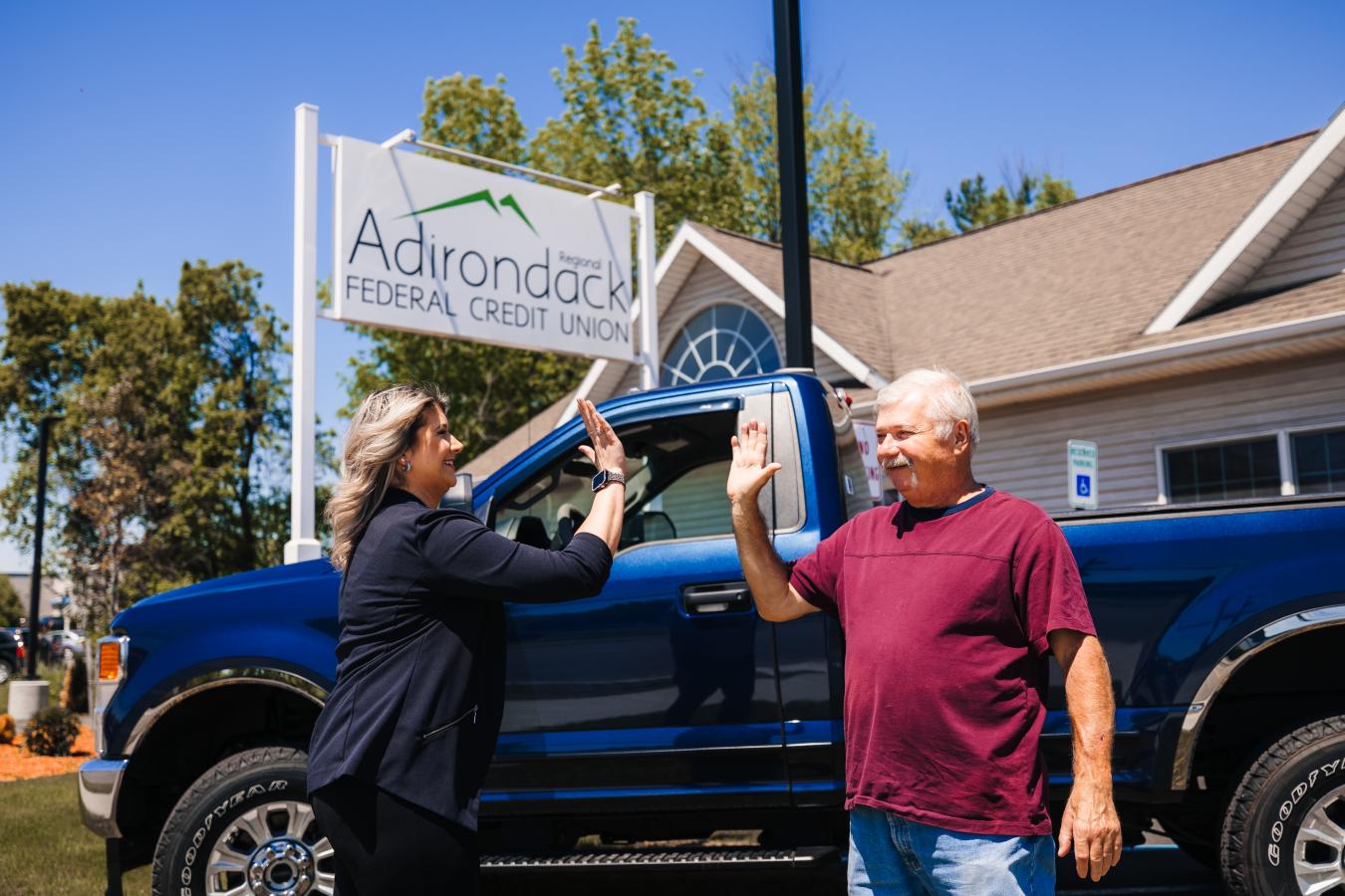 Plattsburgh credit union member high fiving an employee in front of their new truck and the Adirondack Regional Federal Credit Union sign