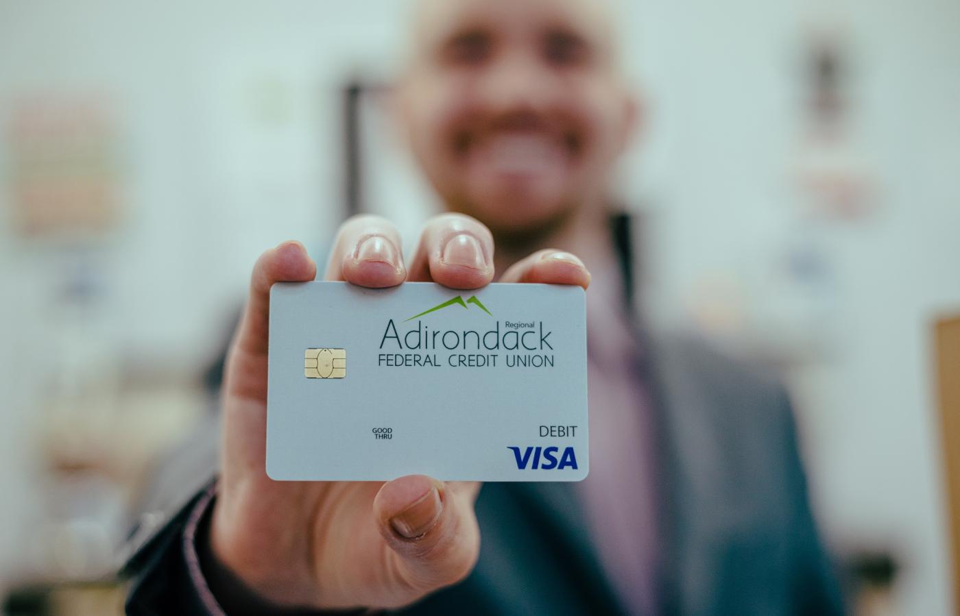 Happy teller holding an Adirondack Regional Federal Credit Union branded debit card
