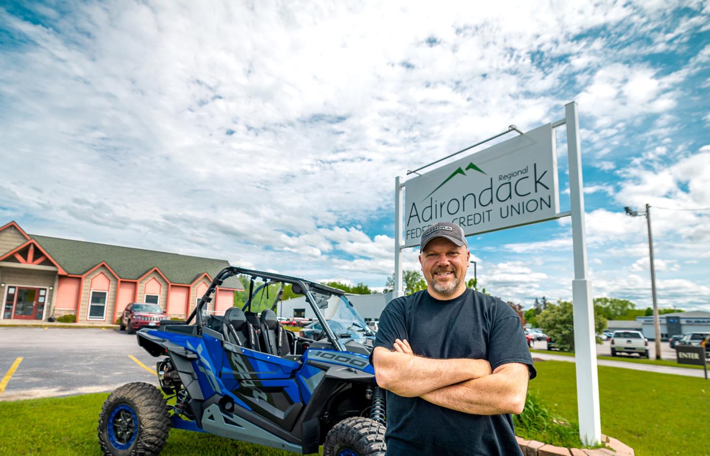 man standing in front of the Adirondack Regional Federal Credit Union sign with a recreational vehicle he bought with a ATV loan from the credit union