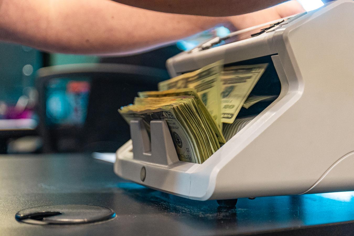 Person operating a money counting machine full of 20 dollar bills