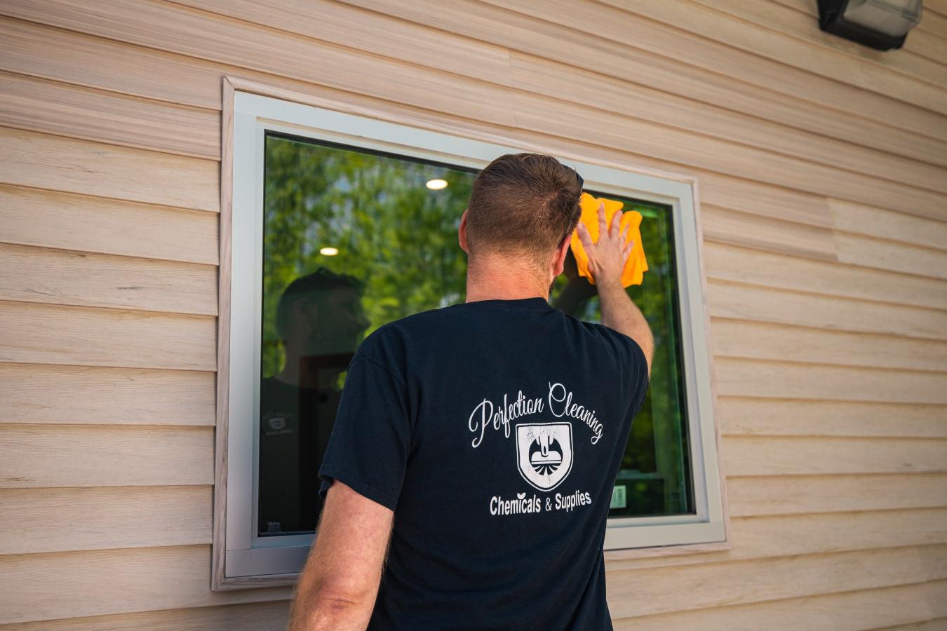 Ian Christensen, owner of Perfection Cleaning wearing a black branded shirt and washing an outer window at Adirondack Regional Federal Credit Union in Plattsburgh