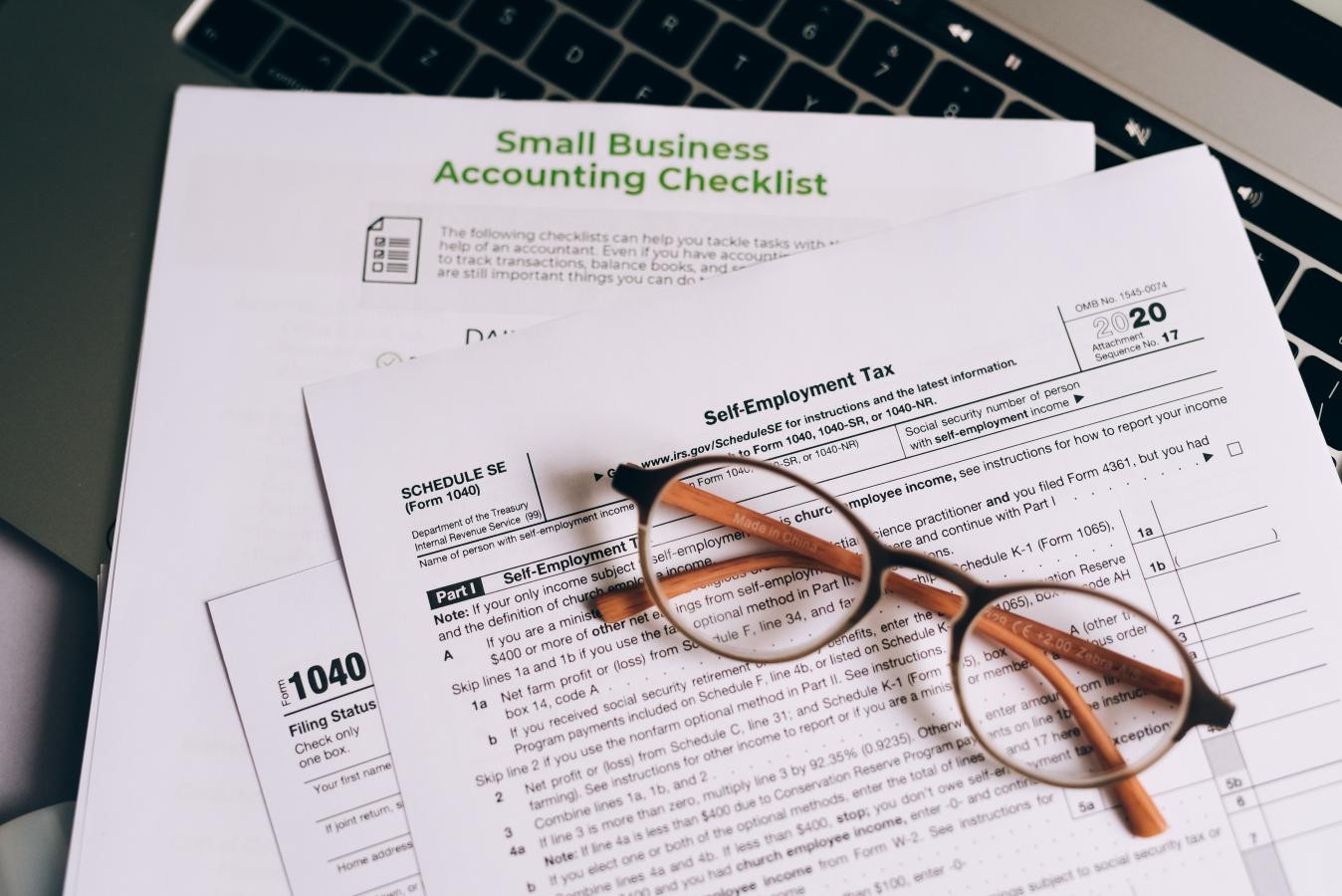 A stack of tax forms on a table with a pair of eyeglasses.