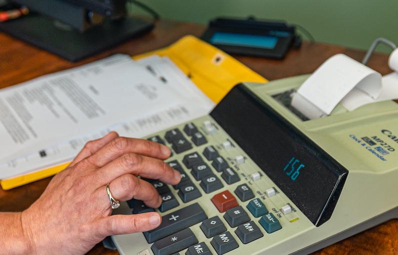 Close up on a hand operating a calculator that prints receipts. A number of bank documents are next to the calculator.