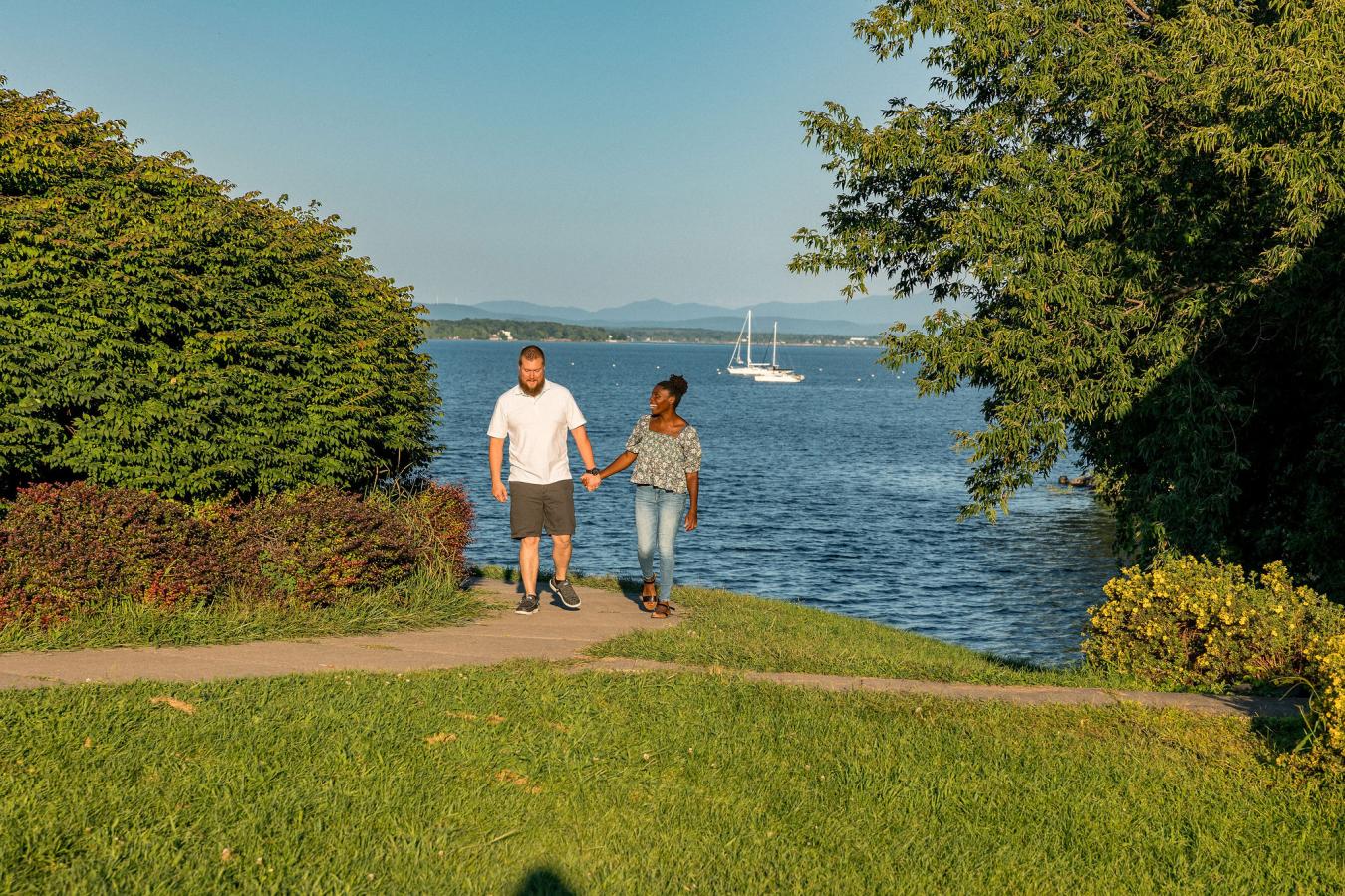 Couple walking through park with sail boats in background.