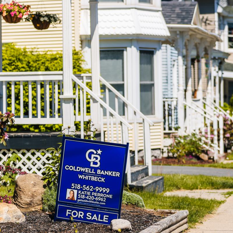 Blue Coldwell Banker Whitbank Real Estate Sign in front of a Plattsburgh NY home for sale