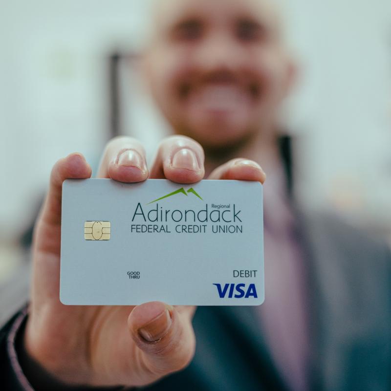 Employee holding up an Adirondack Regional Federal Credit Union branded Visa credit card