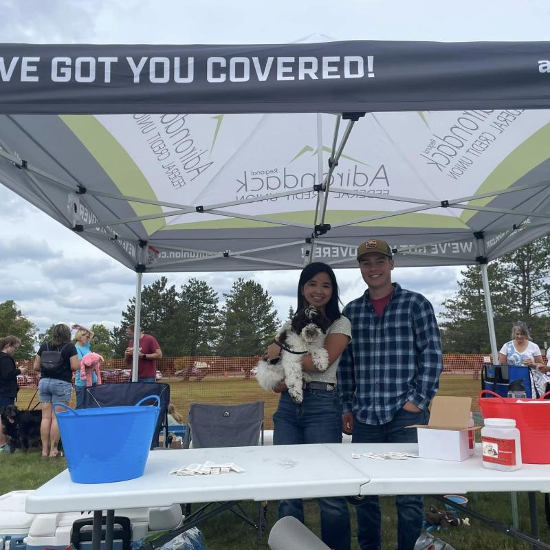 Two event staff holding their dog as they stand under a tent