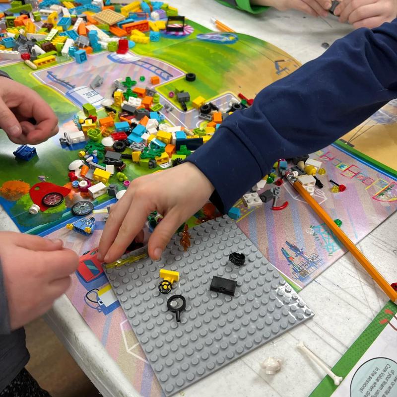 Children's hands building a Lego structure.
