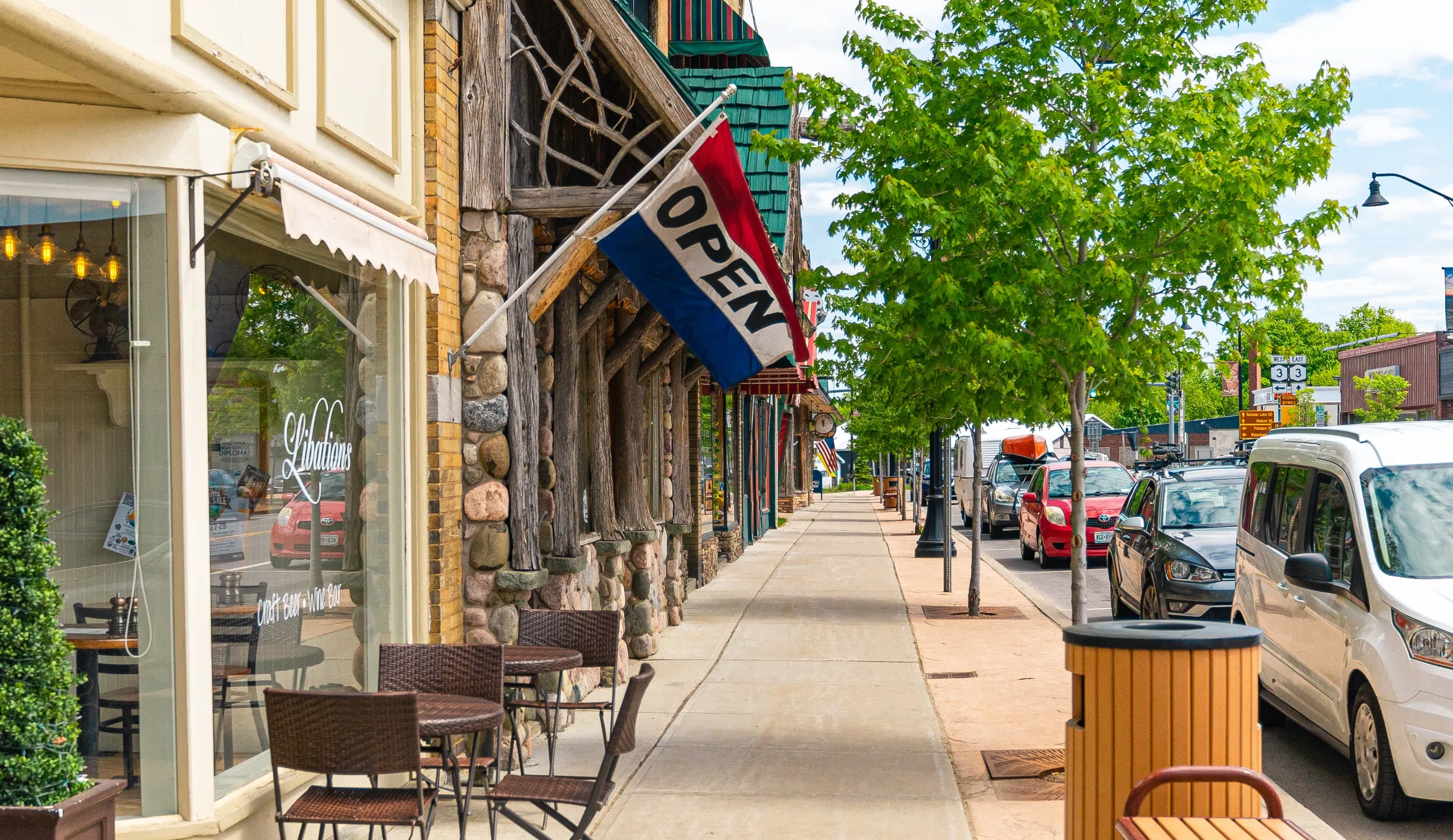 Sidewalk lined with small businesses with an "open" flag.