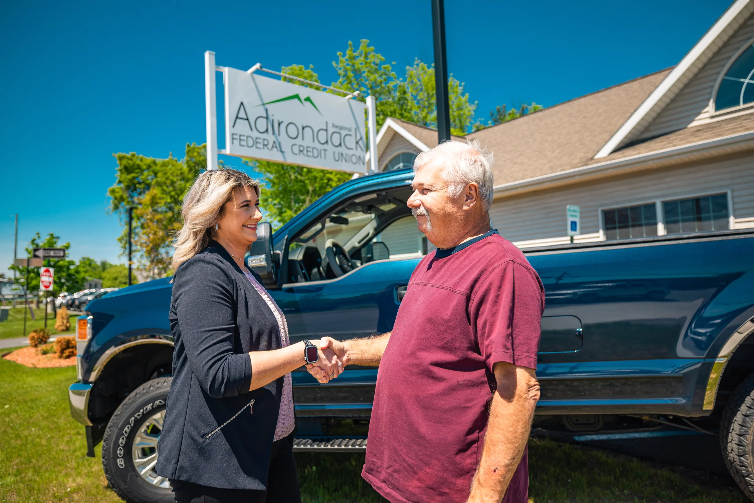 Two people shaking hands in front of a blue truck. 