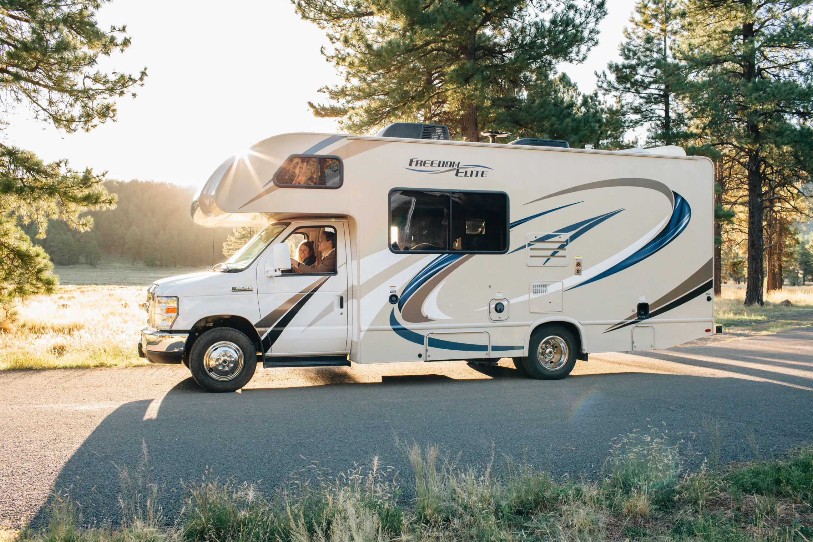RV parked on a road, surrounded by woods.
